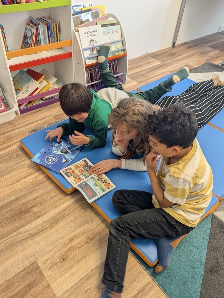 Une adulte et deux enfants qui lisent ensemble à l'école